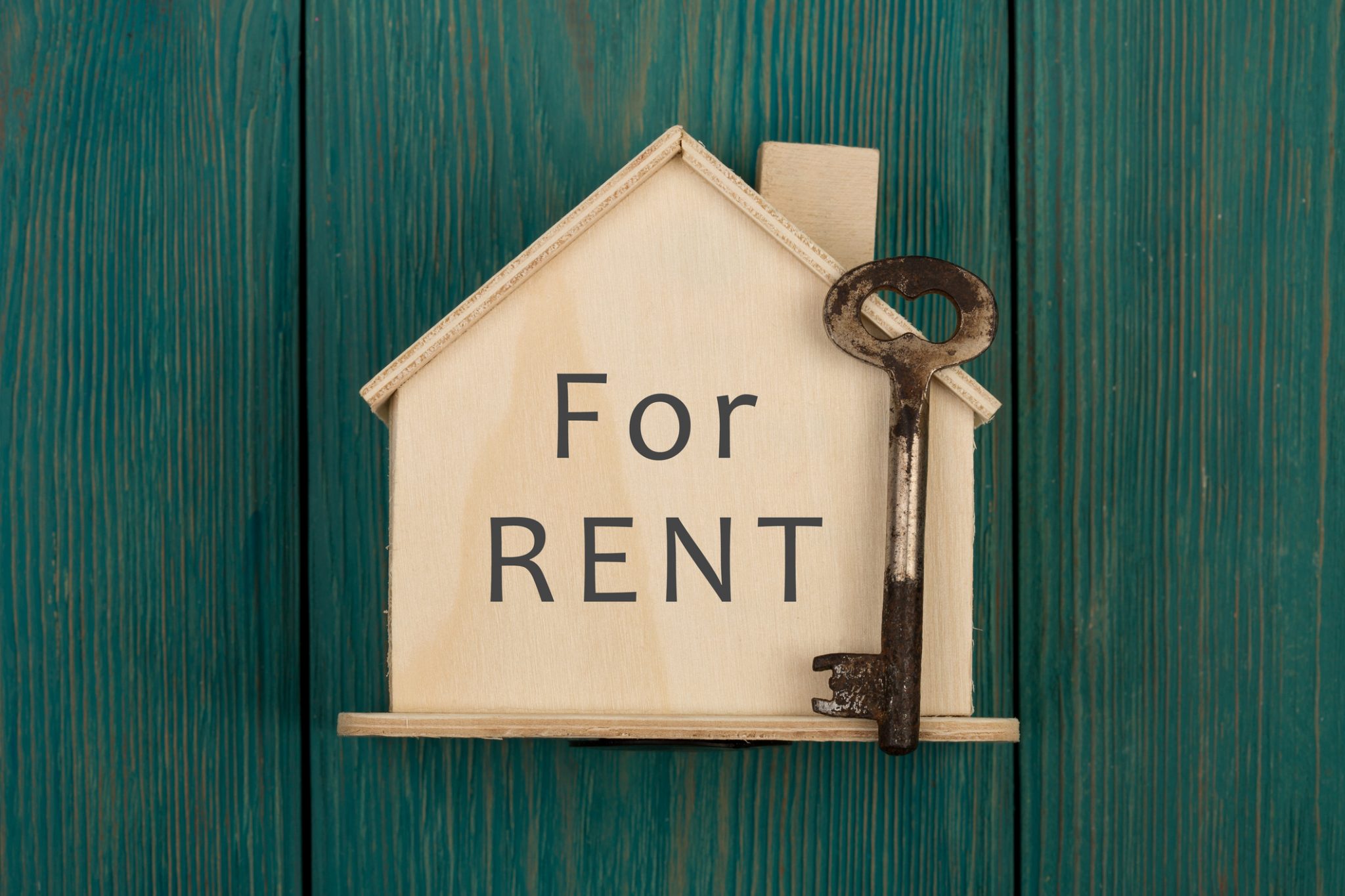 Little house with text "For rent" and key on blue wooden background